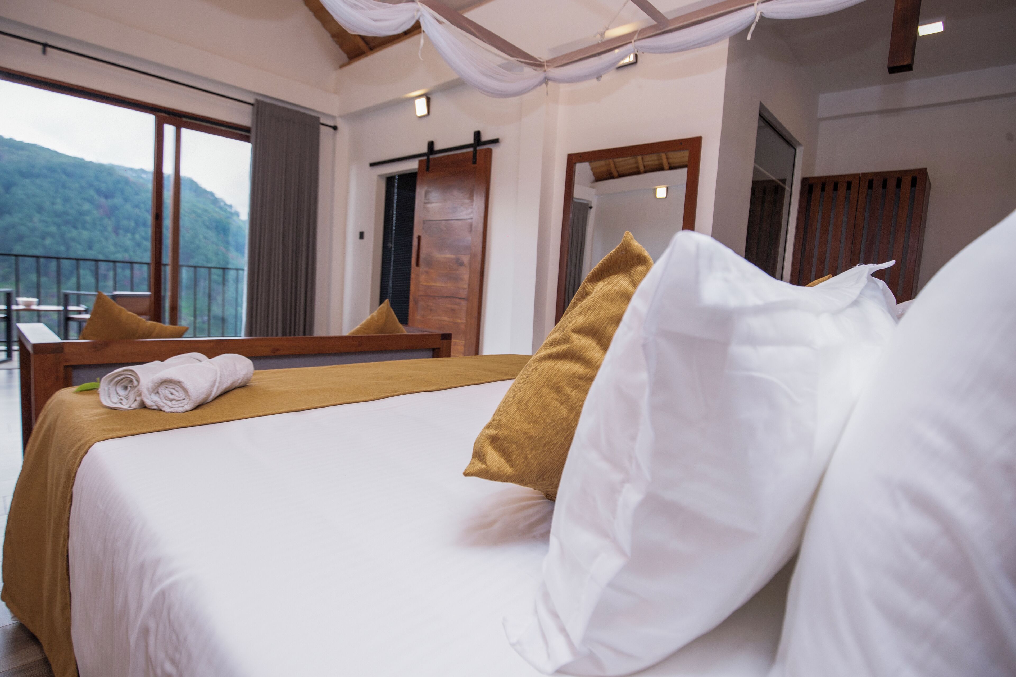 A hotel room with a large bed, a balcony with a view of the mountains, and a wooden door.