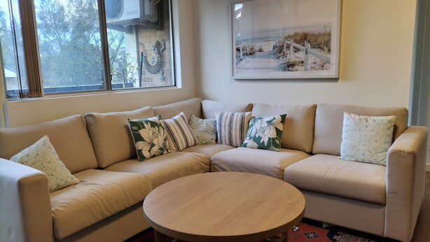 A living room with a beige sectional sofa, a round wooden coffee table, and a framed picture on the wall.