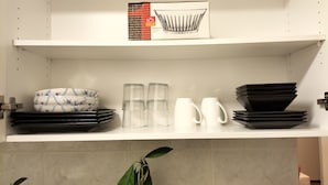 A kitchen shelf with stacked plates, bowls, glasses, and a white mug.