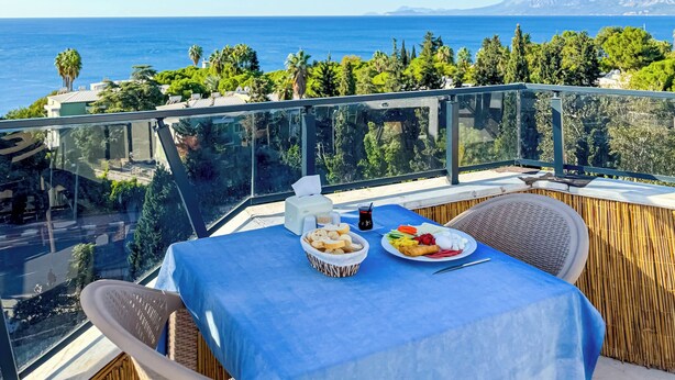 A balcony with a table set for a meal, overlooking a coastal view with mountains in the distance. - Deluxe Ersoy Hotel (Antalya)