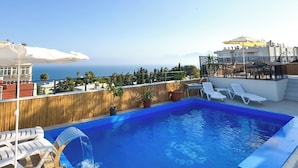 A rooftop pool with clear blue water, white lounge chairs, and a view of the ocean. - Deluxe Ersoy Hotel (Antalya)