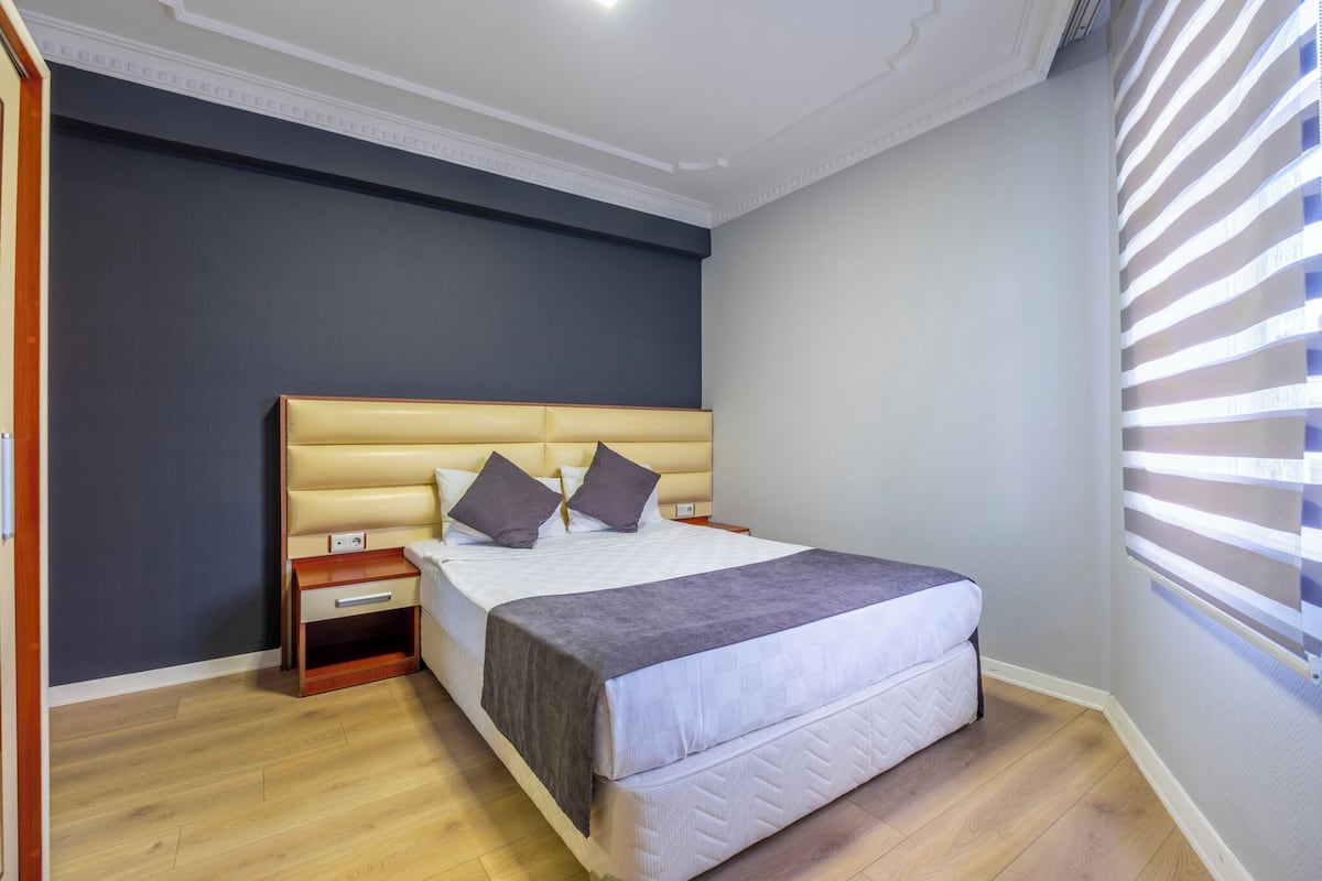 Une chambre à coucher avec un grand lit, une table de chevet et une fenêtre avec des stores.