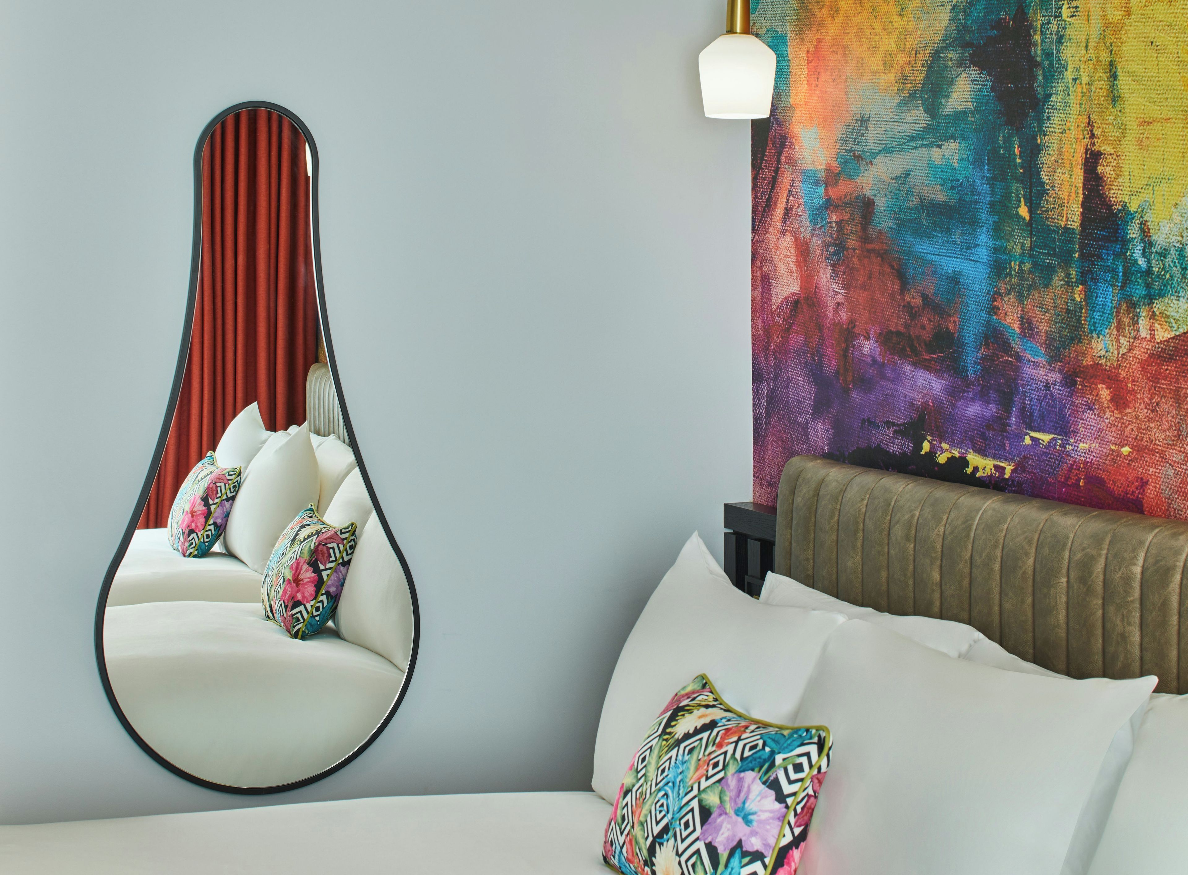 A room with a hanging chair, a colorful abstract painting, and a bed with patterned pillows.
