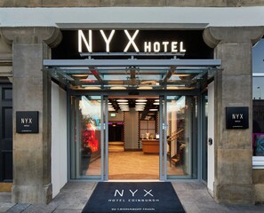 L’entrée de l’hôtel NYX à Édimbourg se distingue par sa façade moderne en verre, son comptoir d’accueil et son intérieur visible à travers le verre.