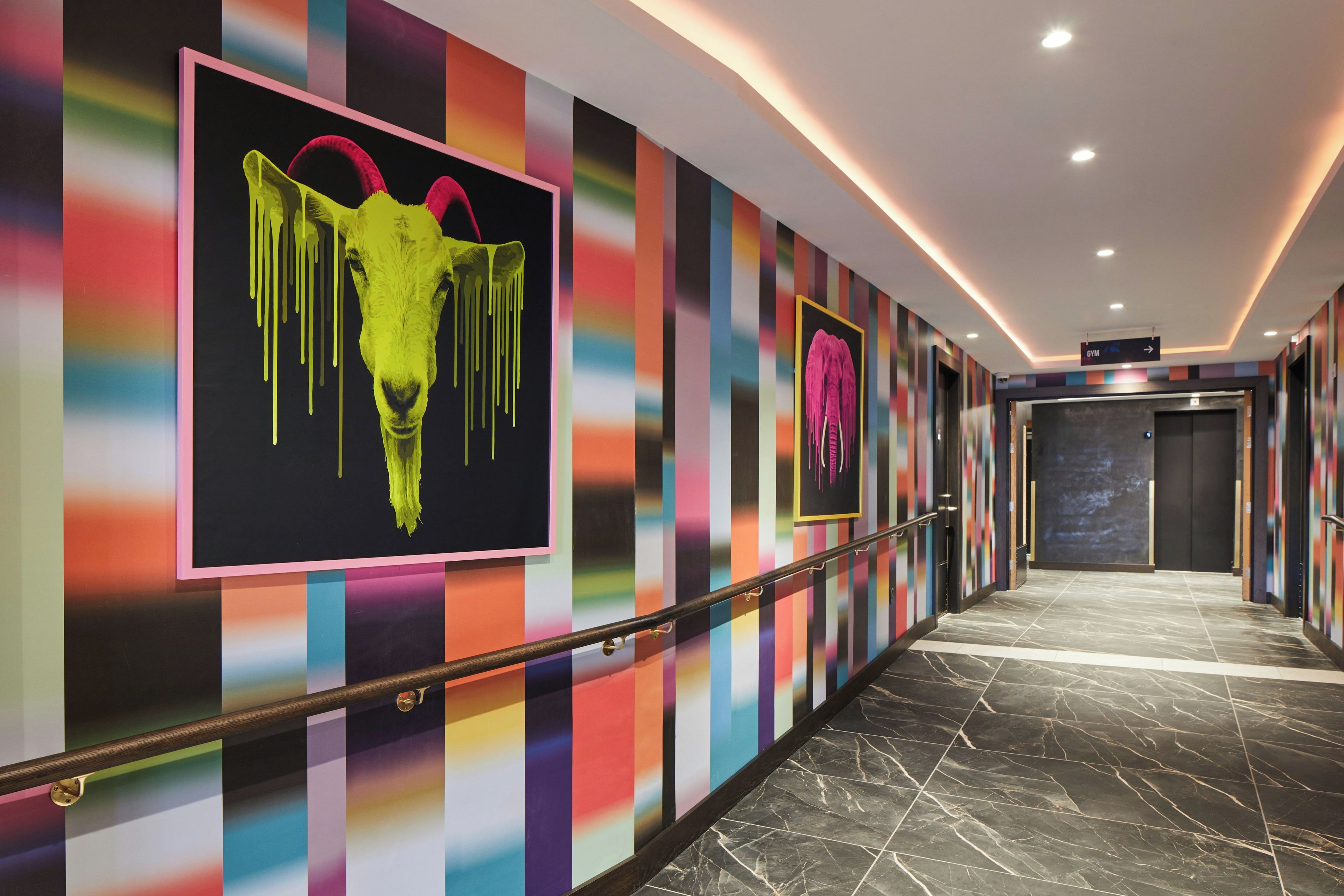 A hallway with colorful striped walls, a marble floor, and a sign indicating a gym.