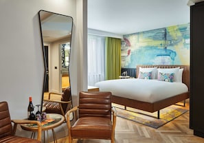 A hotel room with a large bed, a sitting area with a chair and table, a large mirror, and a colorful abstract painting on the wall. - NYX Hotel Edinburgh by Leonardo Hotels (Edinburgh)