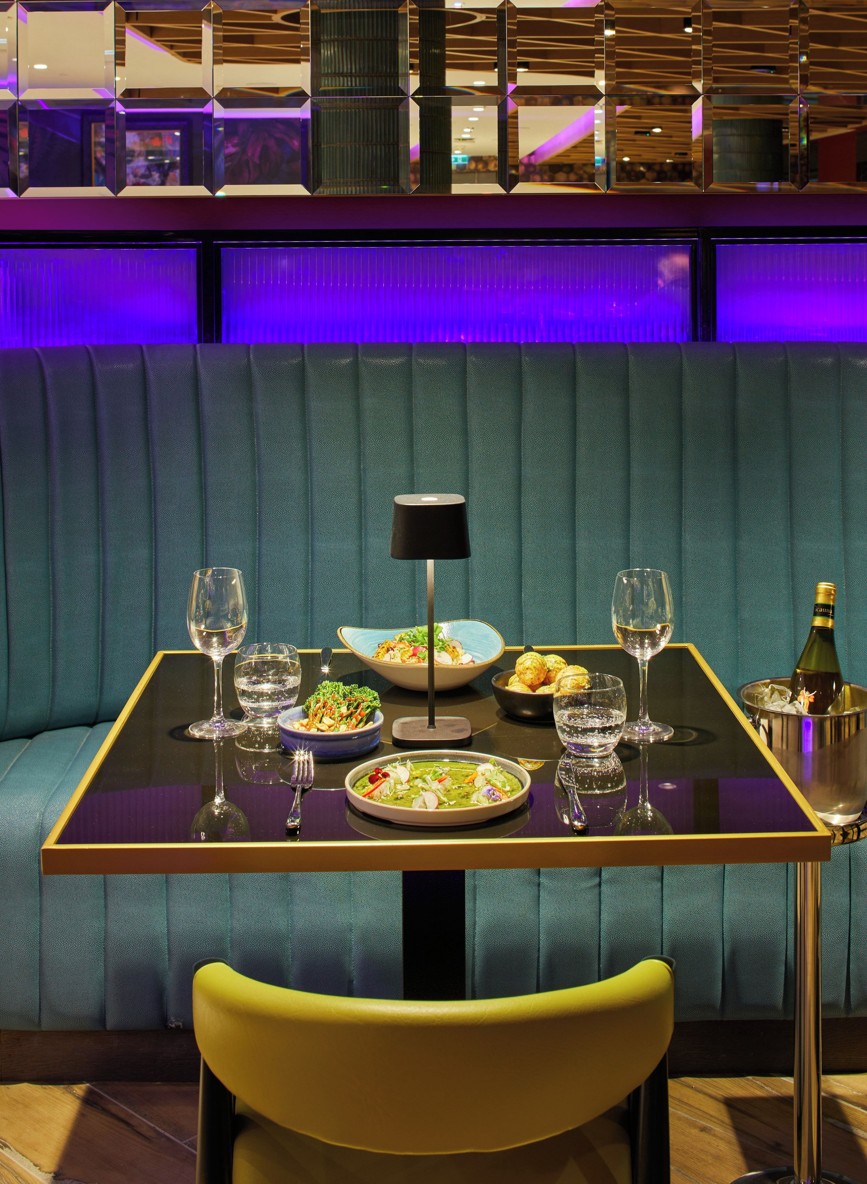 A dining table set with a bottle of champagne, glasses, and plates of food.