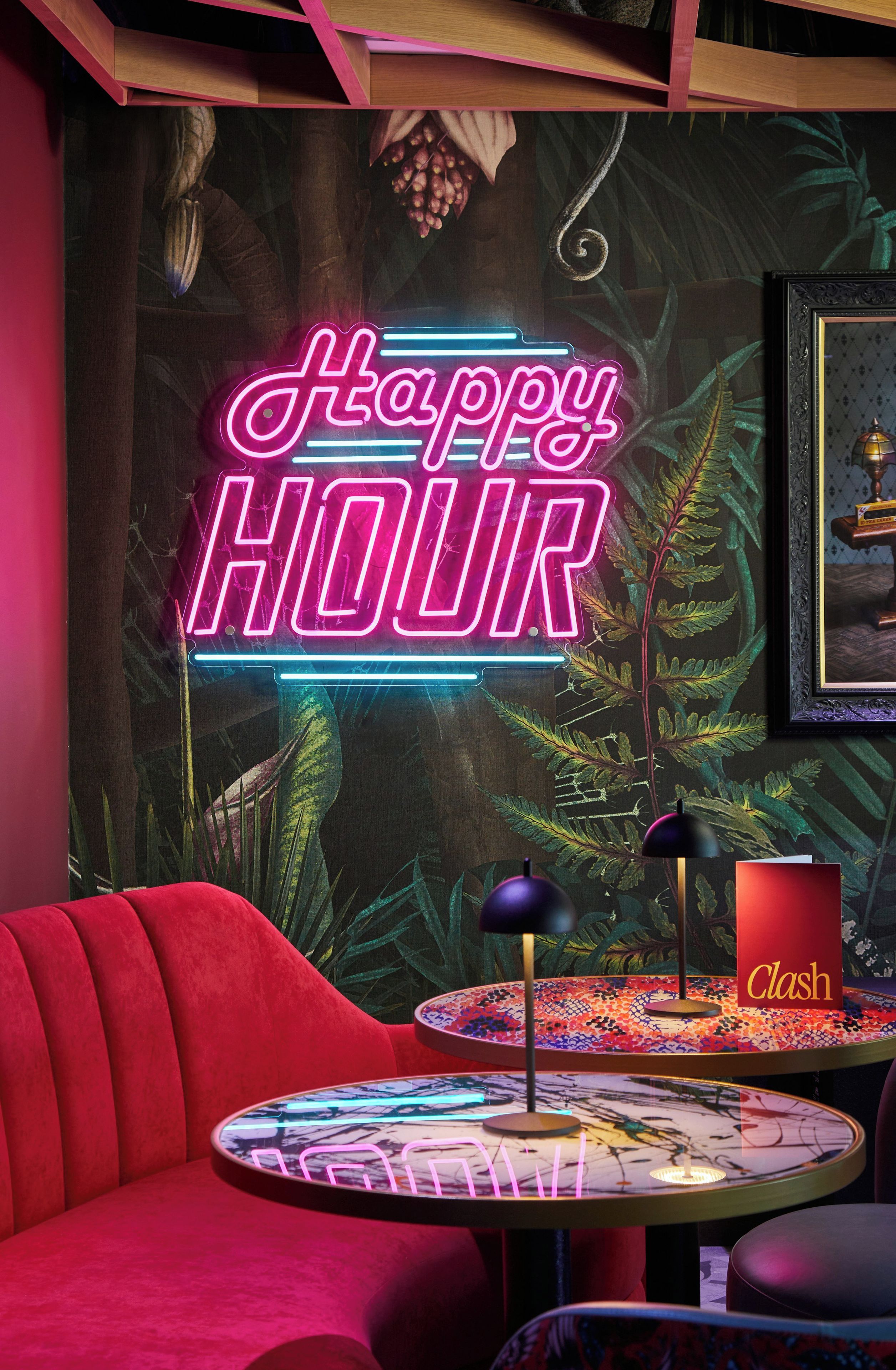 A neon sign reading 'Happy Hour' in a room with a red couch, a small round table with a colorful mosaic, and a framed picture on the wall.