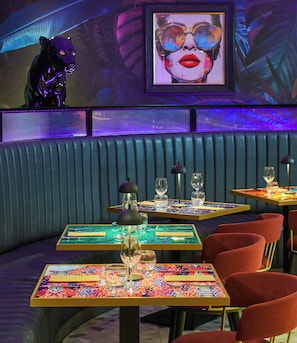 Interior de un restaurante con cabinas, mesas y una pantalla grande mostrando una imagen.