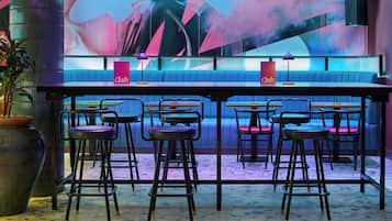 Zona de bar con taburetes y una barra, un mural abstracto de gran tamaño en la pared y una planta en maceta.