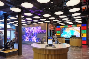 Una moderna zona de recepción con un mostrador central, grandes pantallas digitales e iluminación circular en el techo.