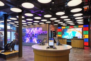 A modern reception area with a central desk, large digital screens, and a ceiling with circular lighting fixtures.