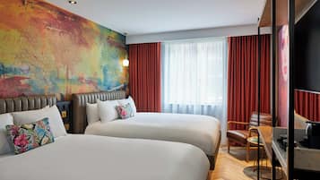 Habitación de hotel con dos camas, un cuadro abstracto grande en la pared, un escritorio con una silla y vistas de la ciudad a través de amplias ventanas.