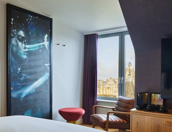 A hotel room with a large window, a bed, a red stool, a brown leather chair, and a coffee station. - NYX Hotel Edinburgh by Leonardo Hotels (Edinburgh)