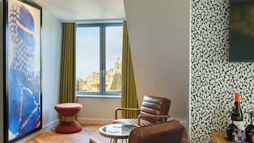 A modern living room with a city view, a red stool, leather chairs, and a table with a glass top.