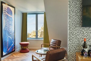 Een moderne woonkamer met uitzicht op de stad, een rode kruk, lederen fauteuils en een tafel met een glazen blad.