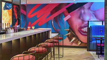 Uma área de bar com design moderno, destacando um balcão com tela digital, banquetas e um grande mural abstrato na parede.