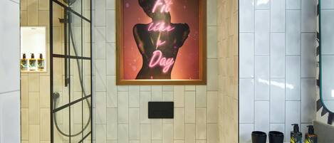 Un baño con ducha, lavamanos y una obra de arte enmarcada en la pared.