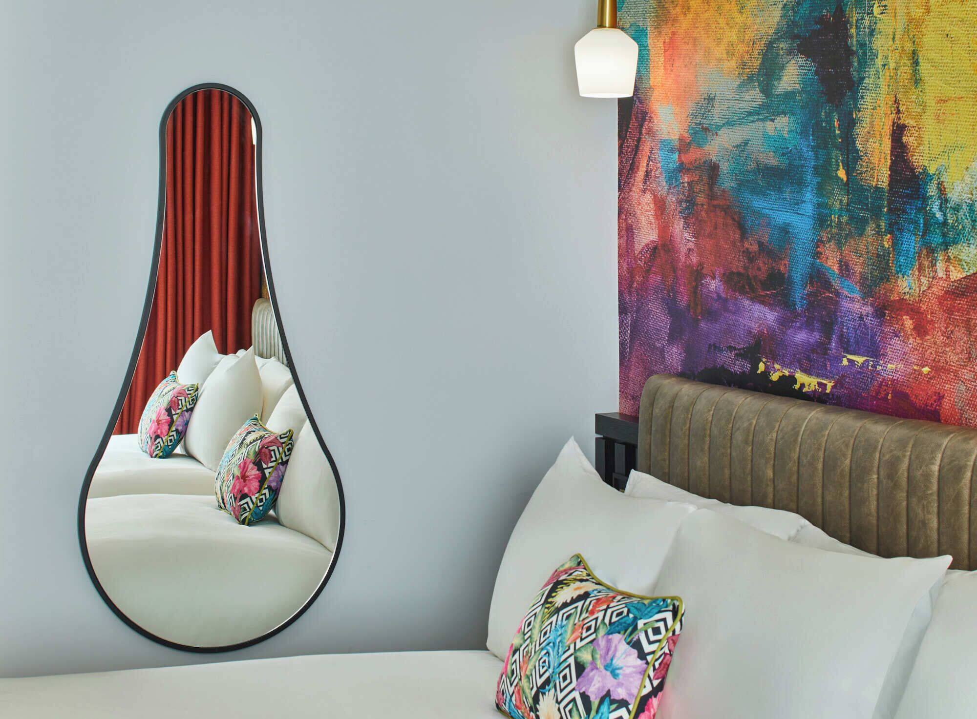 Une chambre moderne avec un fauteuil suspendu, un tableau abstrait aux couleurs vives et un canapé agrémenté de coussins à motifs.