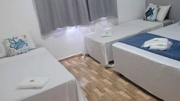 Habitación de hotel con dos camas individuales, una mesita, un calentador en la pared y una ventana con cortinas grises.