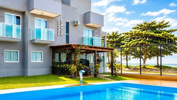 A modern building with a pool, a covered patio, and a view of the sea. - POUSADA SOL & MAR (Serra)