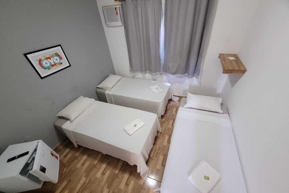 A room with two single beds, a wooden floor, a small table, and a wall-mounted air conditioning unit.