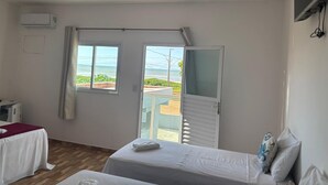 A room with two beds, a window with a view of the beach, and an air conditioning unit. - POUSADA SOL & MAR (Serra)
