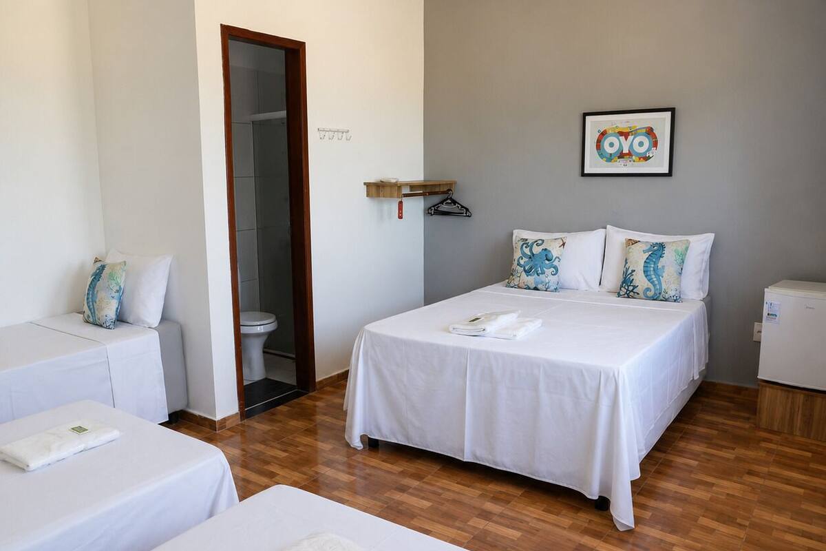 A hotel room with two beds, a small seating area, a toilet, and a refrigerator.
