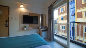 A hotel room with a bed, a desk, a television, a small refrigerator, and a window with a view of buildings. - Olive Hotel Kundalahalli by Embassy Group (Bengaluru)