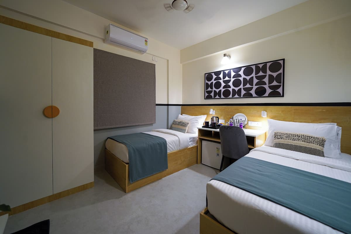 A hotel room with two beds, a desk, a chair, a wardrobe, and a wall-mounted artwork.