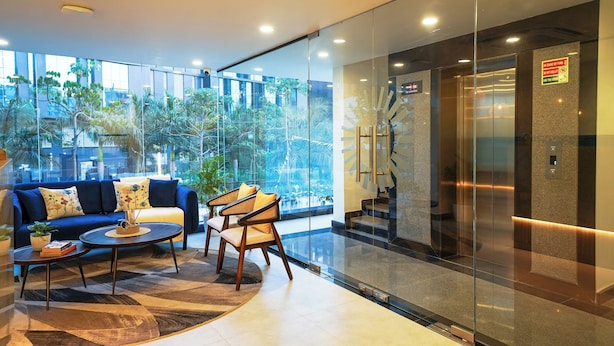 A modern lobby with a blue sofa, two armchairs, a coffee table, and a glass elevator. - Olive Hotel Kundalahalli by Embassy Group (Bengaluru)