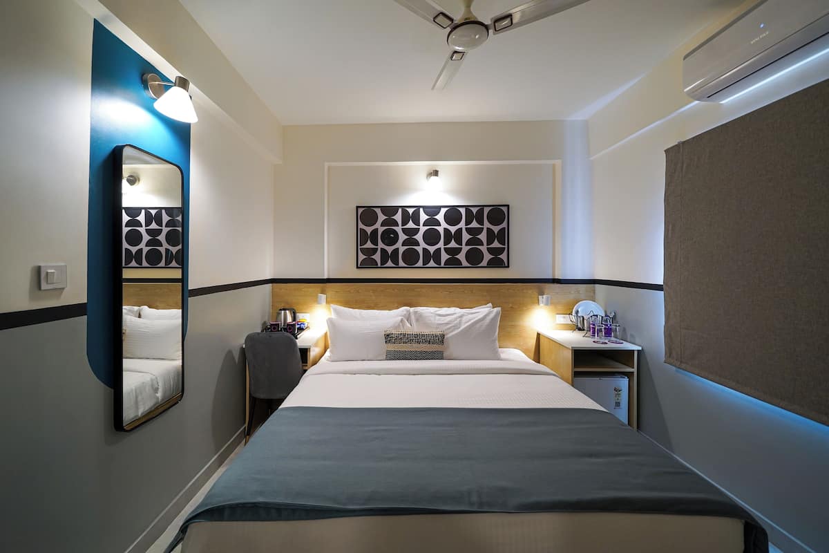 A hotel room with a bed, bedside tables, a mirror, a wall art piece, and a ceiling fan.