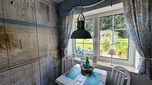 A room with a rustic wooden wall, a table with a map, a hanging lamp, and a view of a garden through a window.