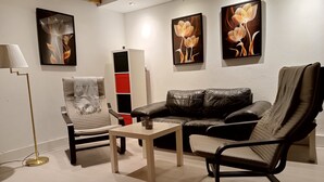 Un salon moderne avec un canapé en cuir, un fauteuil rembourré, une petite table et un lampadaire. Trois œuvres d’art florales encadrées ornent le mur.