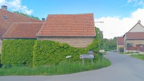 Een landweg met stenen huizen, waarvan er één begroeid is met klimop, en richtingaanwijzingen.