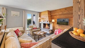 A cozy living room with a fireplace, a sofa set, a dining table, and a kitchen counter with fruit. - Cabane de la Delege -crans Montana- Amazing Views (Lens)