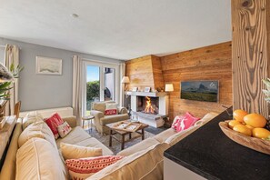 A cozy living room with a fireplace, a sofa set, a dining table, and a kitchen counter with fruit. - Cabane de la Delege -crans Montana- Amazing Views (Lens)