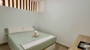 A bedroom with a bed, a ceiling fan, a small wooden table, and a window with vertical blinds. - Apartamento Julia (Costa Adeje)