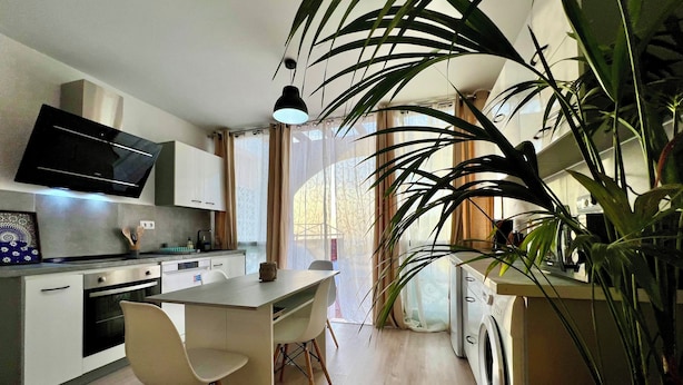 A modern kitchen with a flat-screen TV, a dining area with chairs, and a large potted plant. - Apartamento Julia (Costa Adeje)