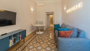 Un salon moderne doté d’un téléviseur à écran plat, d’un canapé avec des coussins, d’une table à manger avec des chaises et d’un sol à motifs.