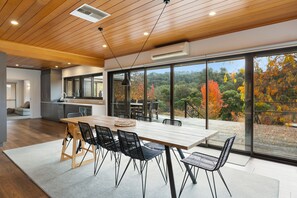 Una cucina moderna con un'isola grande, soffitto in legno e ampie finestre che offrono vista sul fogliame autunnale.