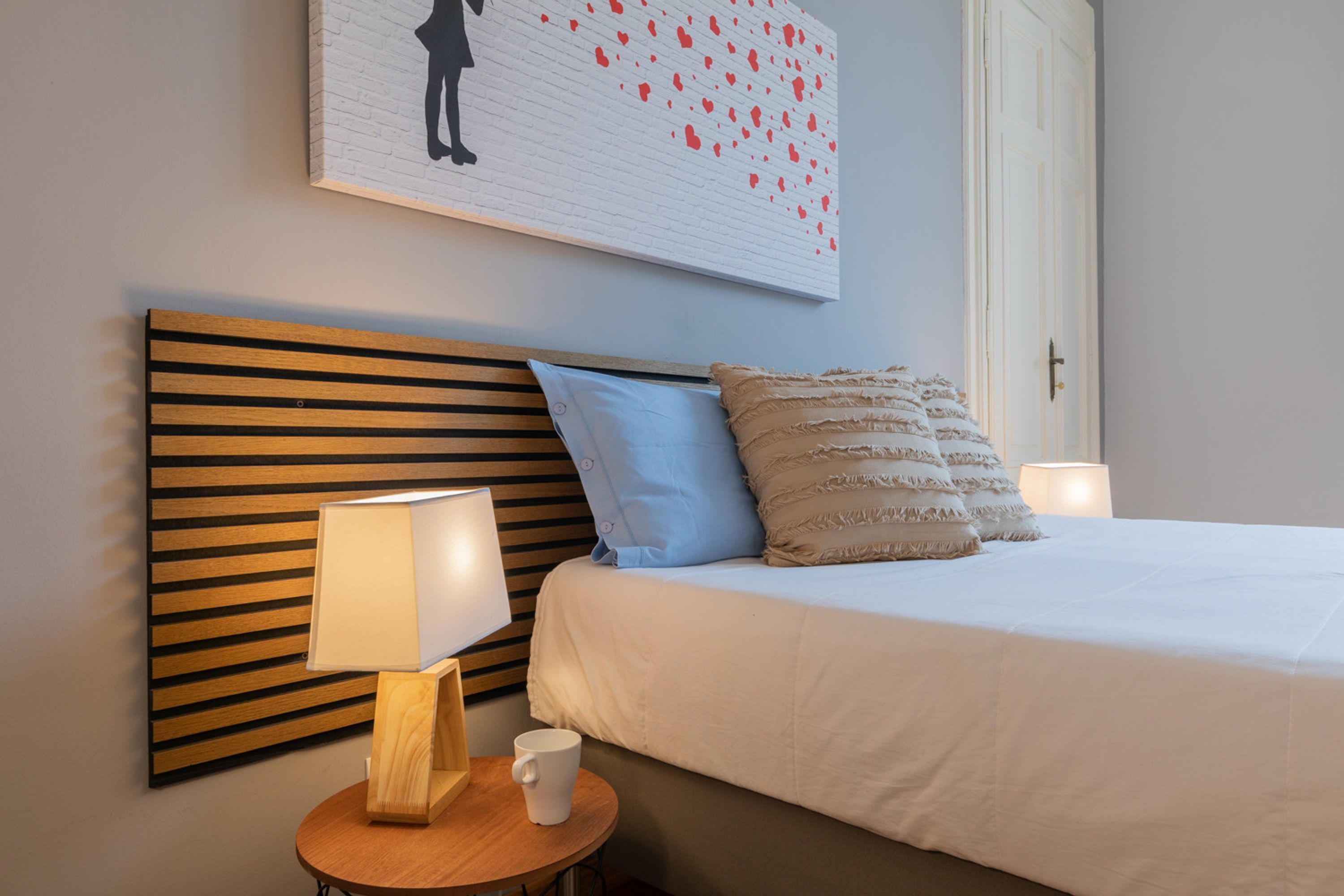 Un lit bien fait, avec une tête de lit en bois, une table de chevet avec une lampe et une œuvre d’art accrochée au mur au-dessus du lit.