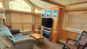 A cozy living room with a sofa, a coffee table, a rocking chair, a TV, and wooden cabinets. - Modern "Tiny Home" Style Cabin on Taylor River with Private Fishing Access (Almont)