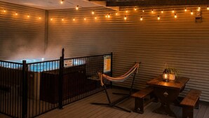 Ett poolområde med en hängmatta, träbänkar, ljusslingor och en bubbelpool.