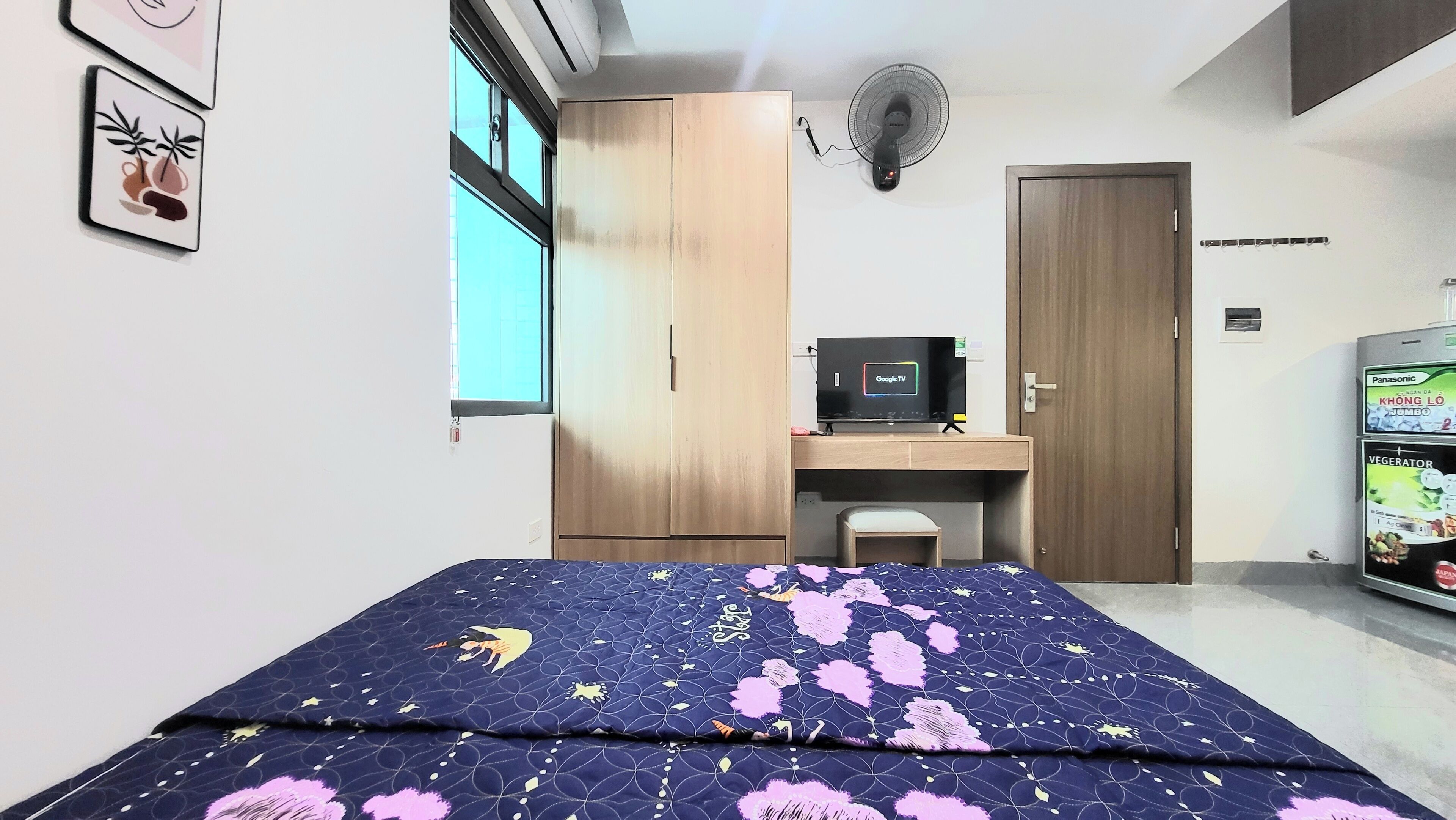 A bedroom with a bed, a desk, a TV, a wardrobe, and a refrigerator.