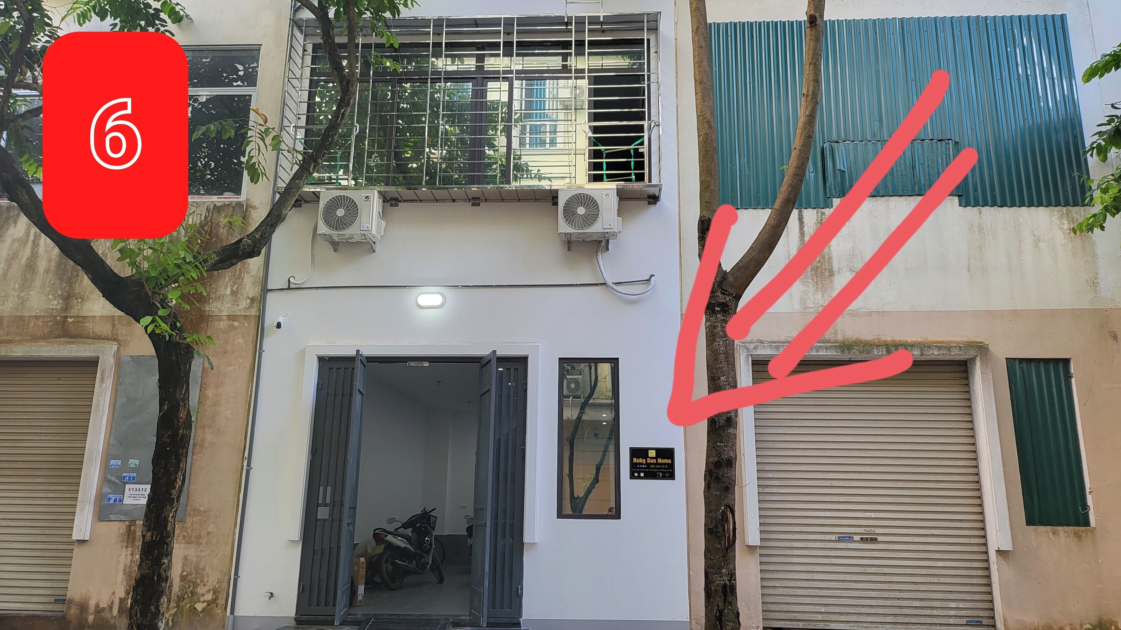 Un bâtiment à la façade blanche, doté d’une fenêtre à cadre métallique et d’un volet métallique fermé sur le côté droit.