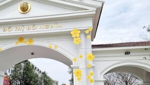 A white building entrance with the text "ĐỘ THỊ ĐỘ NGHỊA" and yellow flowers. - Ruby Sun Home (Hanoi)