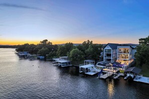A lakeside property with multiple docked boats, a large house with a balcony, and a view of the water. - The High Life | Concierge Services (Kingsland)
