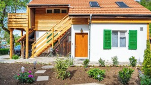 Une maison à deux étages avec un escalier en bois, une petite dépendance en bois attenante et un jardin agrémenté de diverses plantes et fleurs.