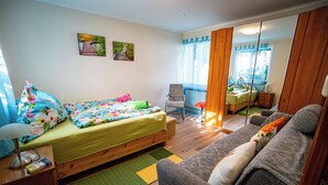 Une chambre à coucher de taille modeste, comprenant un lit simple, un canapé, une chaise et une petite table avec une lampe.